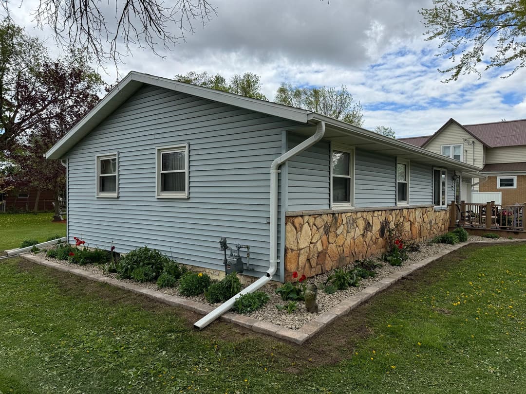 Side view of a light blue house with stone accents and a landscaped garden.
